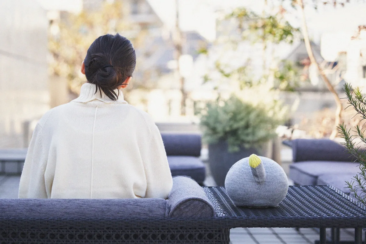 A person relaxing on a sofa beside NICOBO, the companion robot.